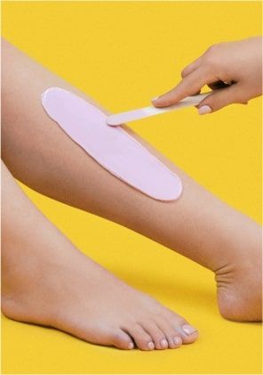 A beautician applies wax to a client's leg